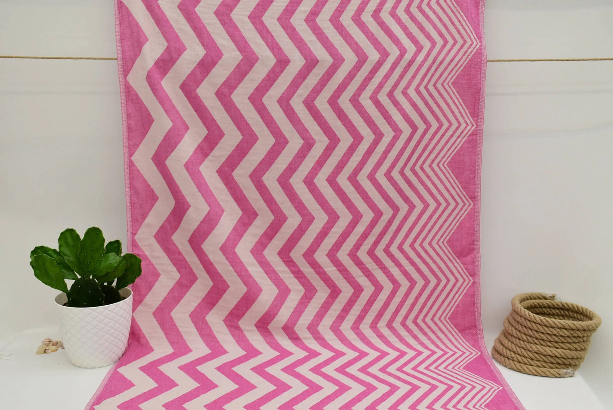 A pink and white zigzag pattern peshtemal towel made of soft textured fabric perfect as a turkish towel