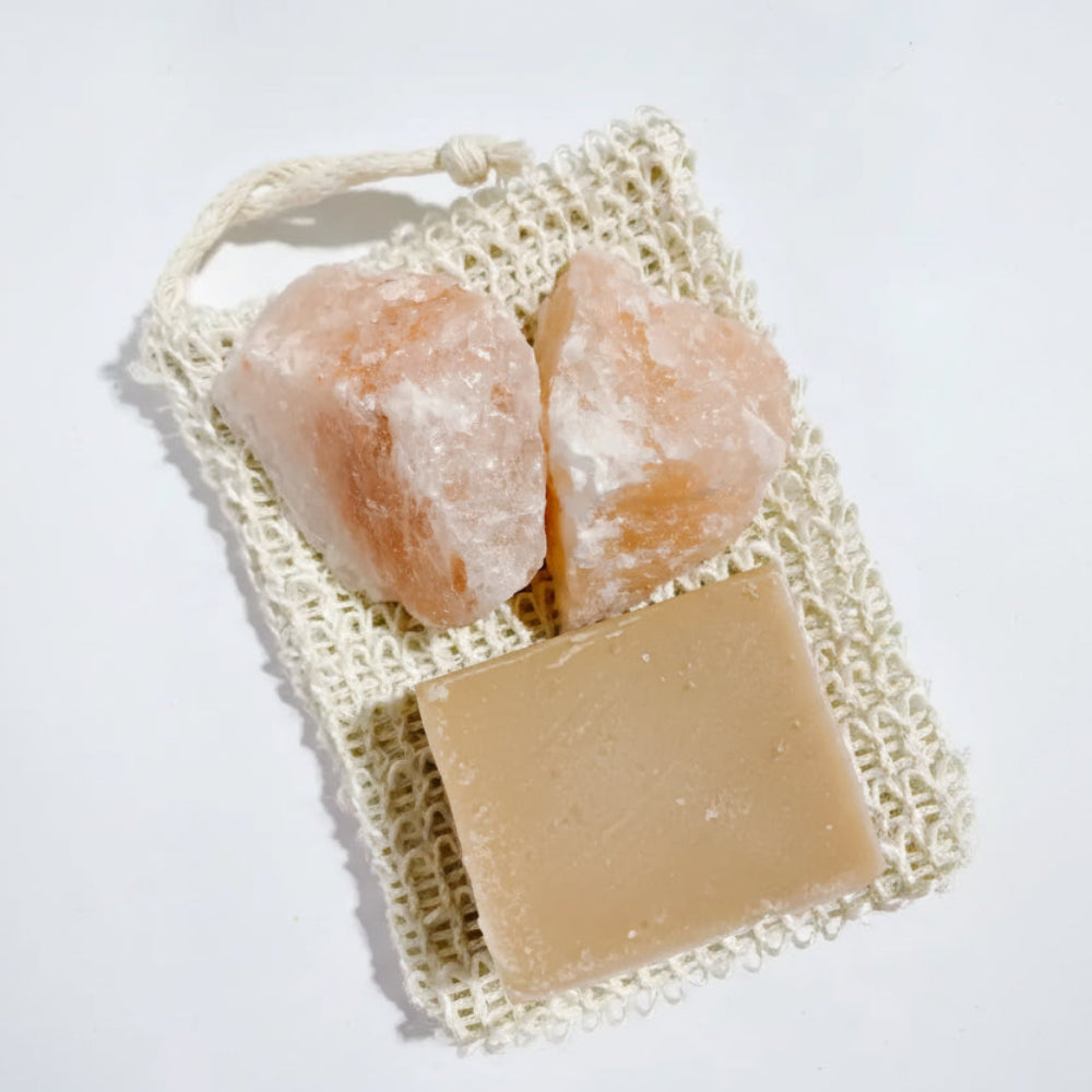 Two pinkish-orange Himalayan salt crystals in cream woven mesh bag with beige soap bar, eco-friendly body scrub