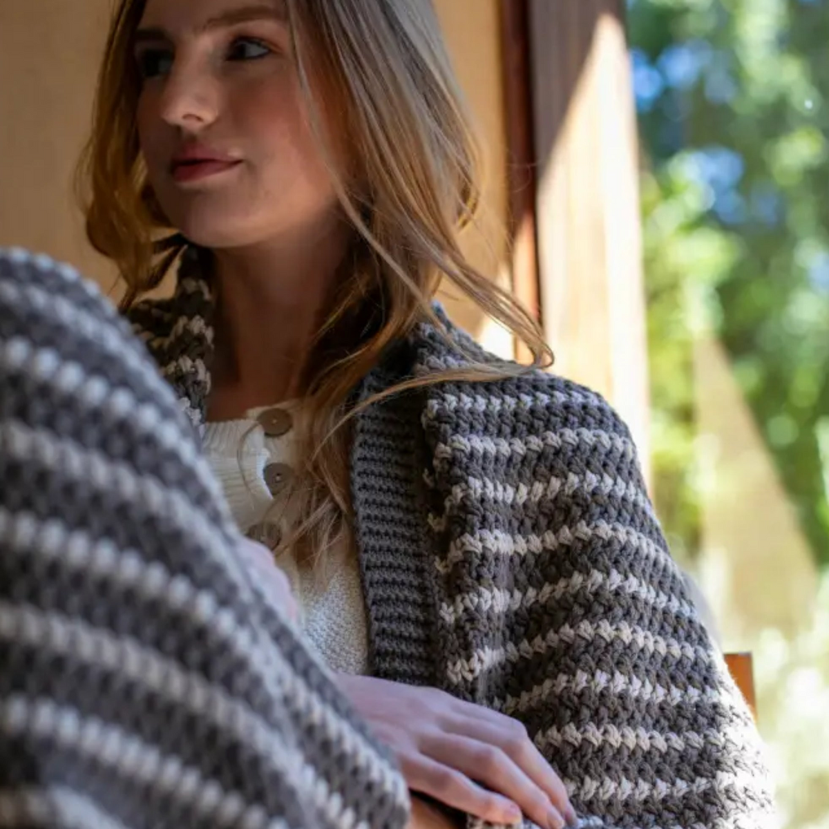 A woman wearing a cozy gray and white organic cotton throw featuring a natural zigzag knit and chunky-knit beauty design