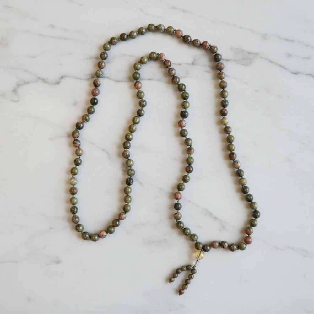 A green unakite mala necklace with 8 mm smooth stones and a beaded tassel designed to support emotional healing