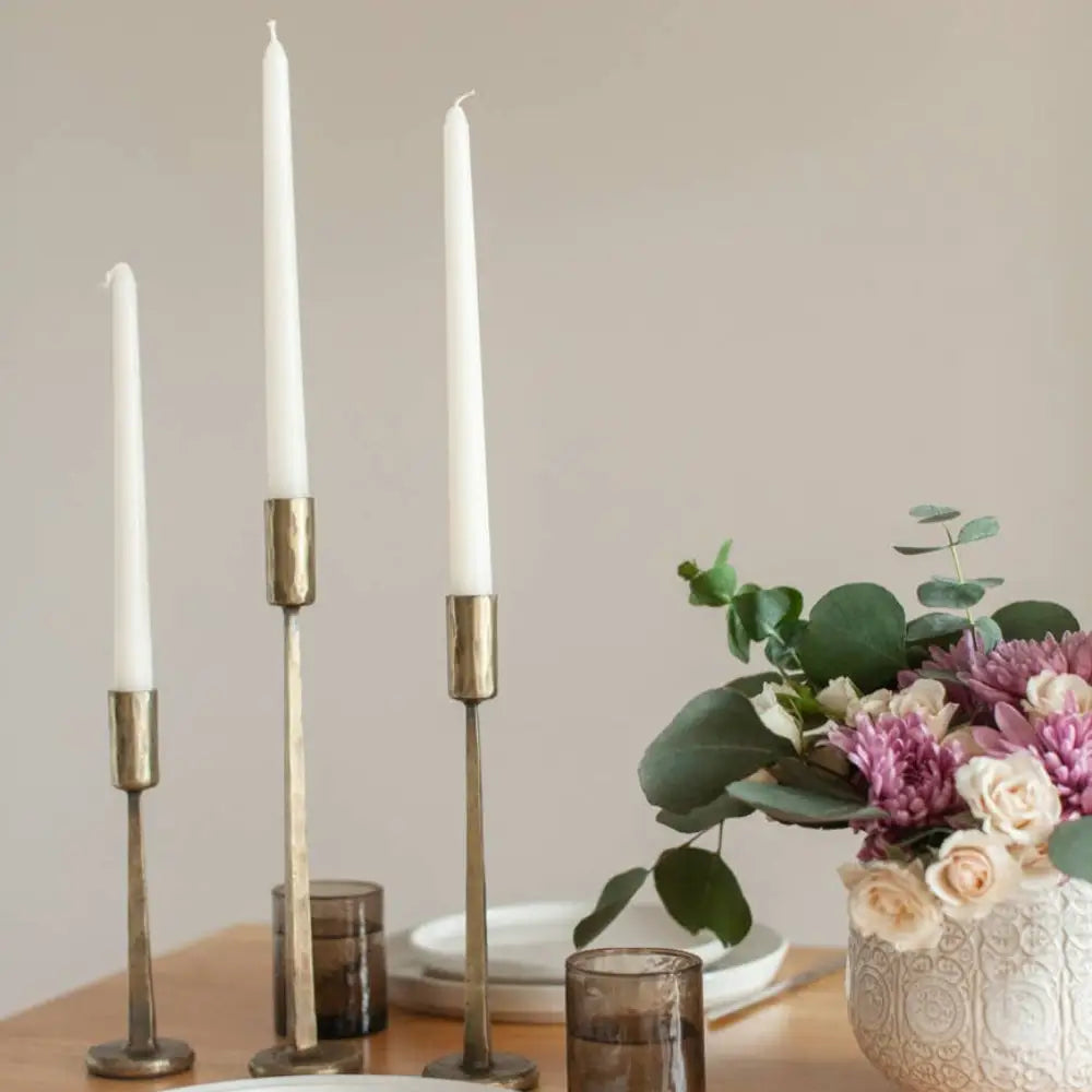 Hand Forged Iron Candle Stands three in brass on wooden table with place setting.