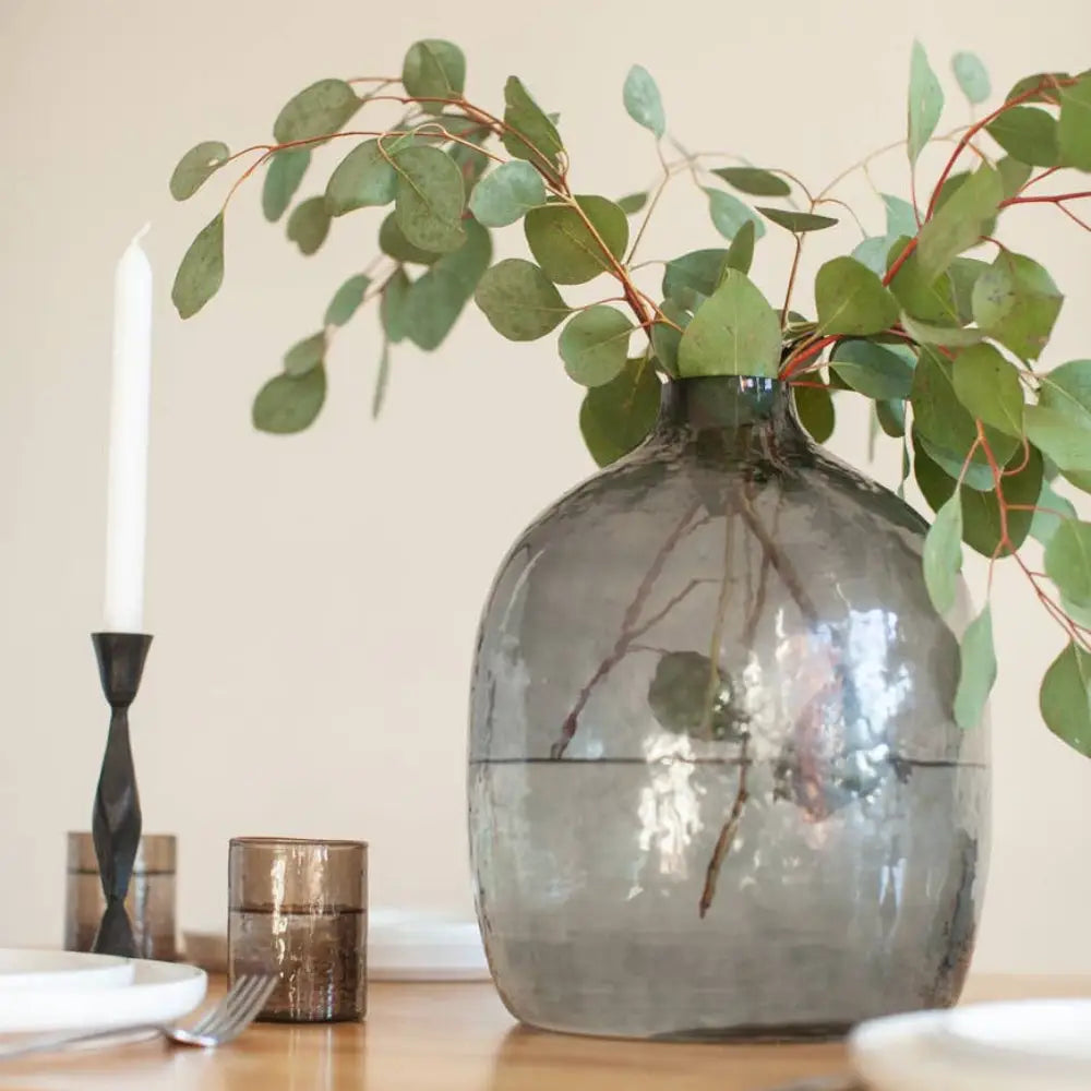 Handblown hammered glass vase in blue gray on wooden table with place setting.