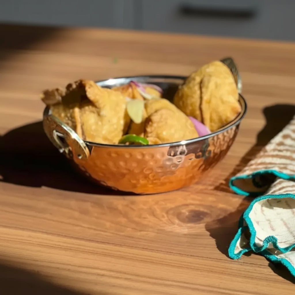 Hammered copper handi double wall serving bowl with brass handles filled with samosas