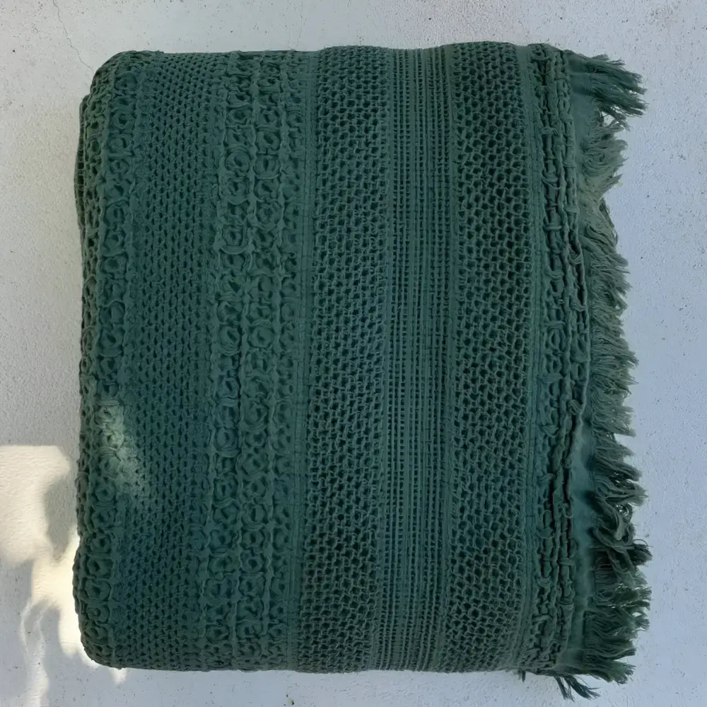 Dark green handwoven waffle bed blanket with fringe edges and textured patterns