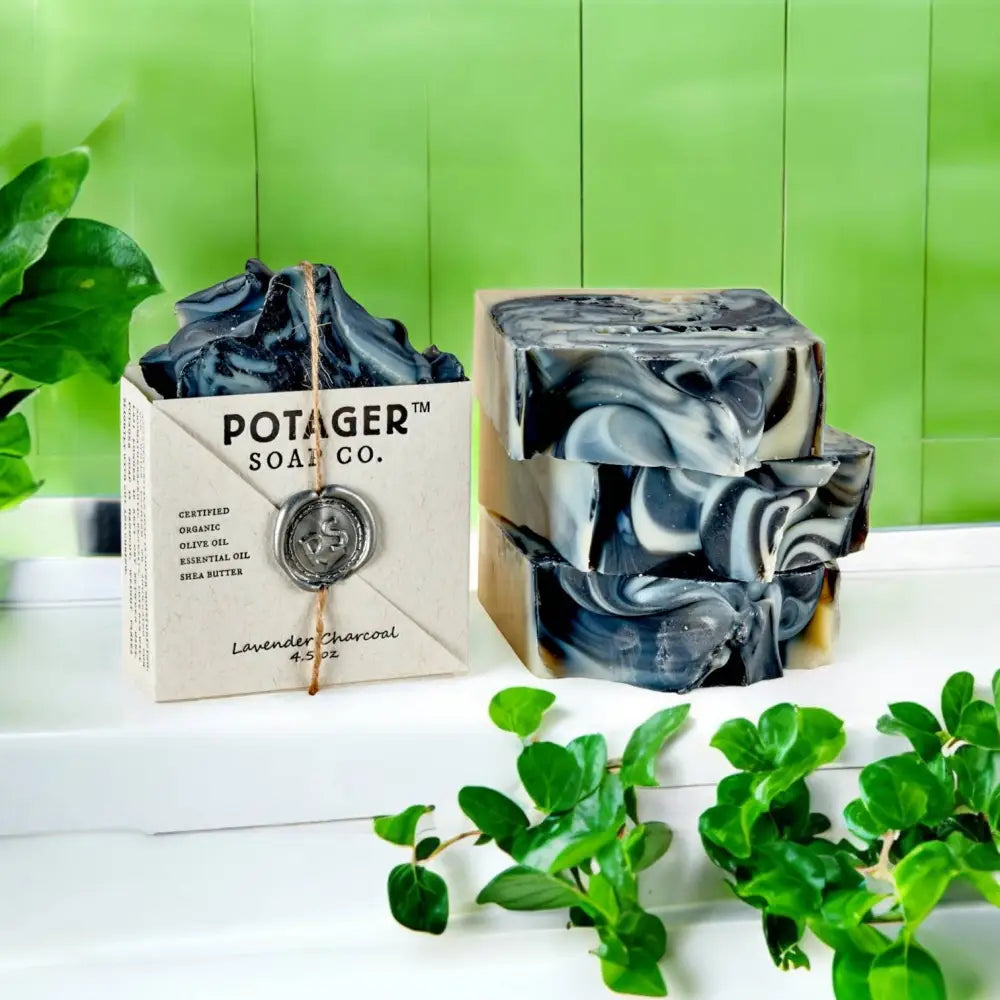 Lavender Charcoal Wrapped soap bar on a white counter surrounded with plants