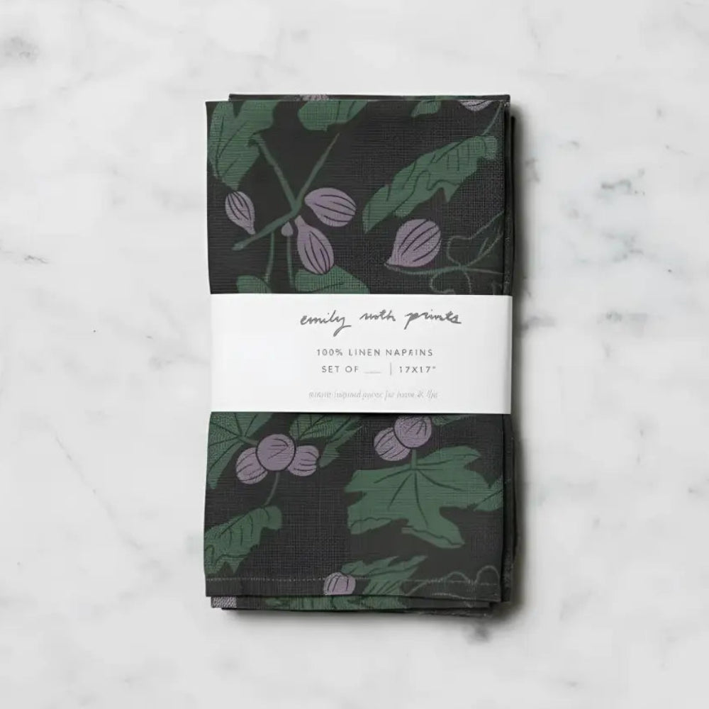 Two linen napkins in dark green with purple fig designs and leaves, wrapped in a white label band