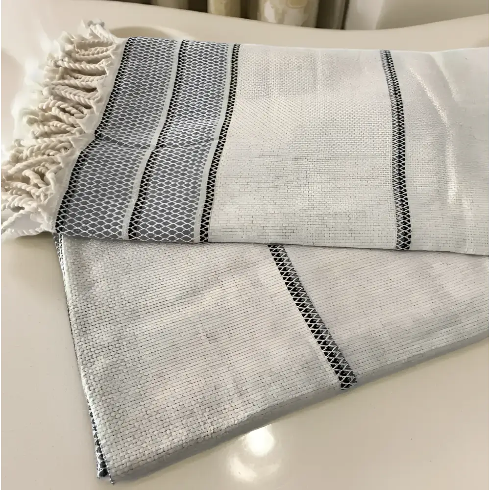 A soft off-white linen turkish bath towel with textured weave gray stripes and black mesh detailing on edges