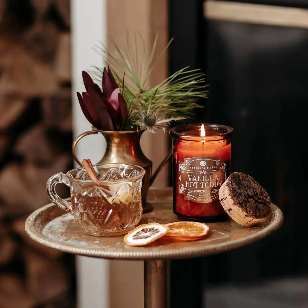 Seasonal Spirit Candles vanilla on a side table with a cocktail and vase of flowers