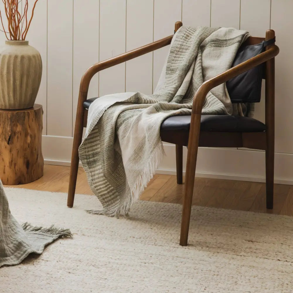 Wooden armchair with leather seat next to a plaid throw blanket in soft ivory and sage green