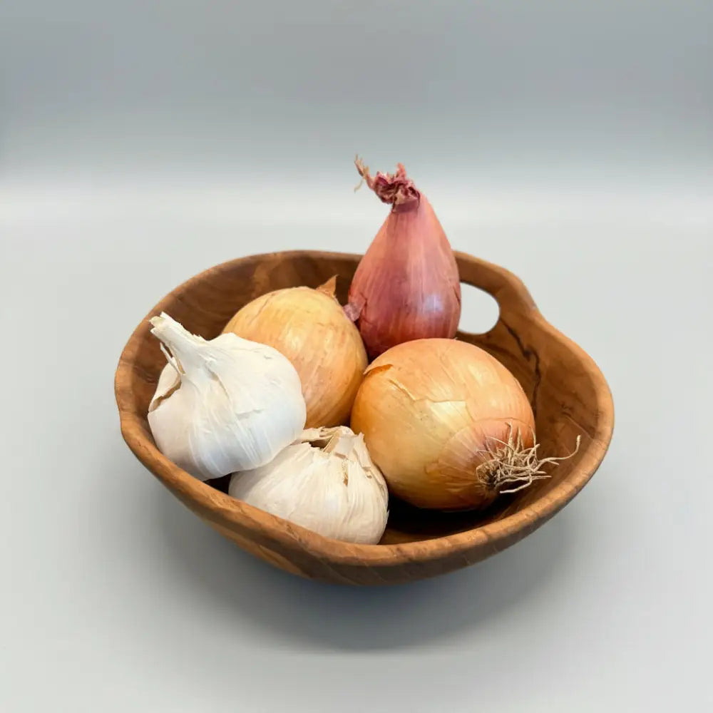 Rustic teak bowl with handles filled with garlic bulbs, yellow onions, and shallots