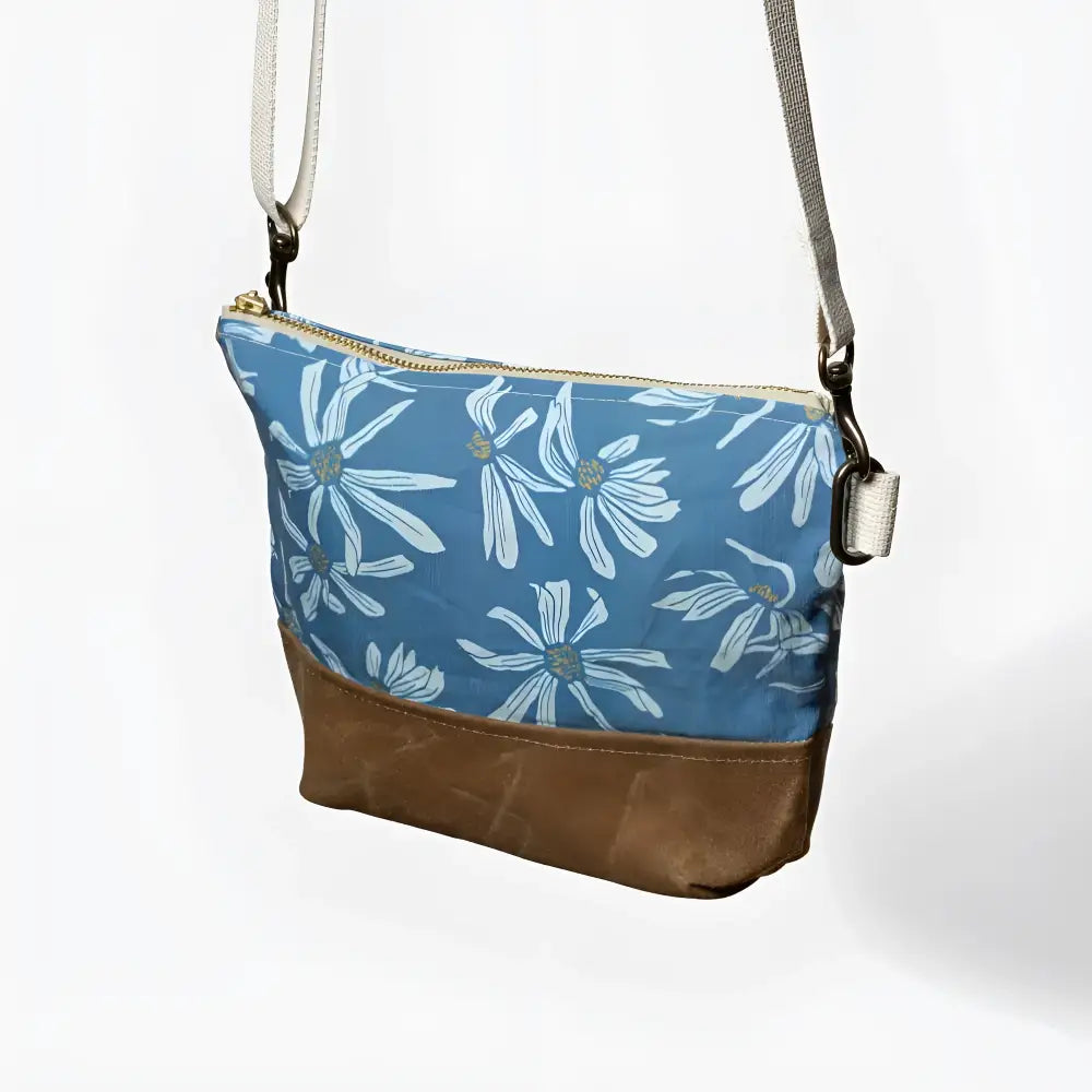Small crossbody bag with blue canvas and white daisy print featuring a brown leather bottom crossbody bag
