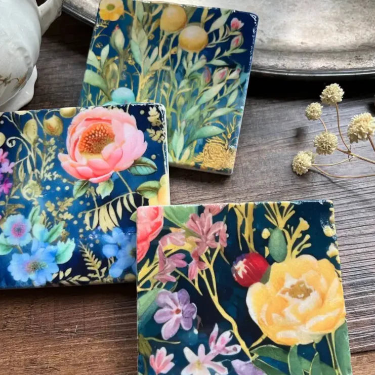 Four Stone Coasters with vibrant watercolor floral patterns on tumbled marble tiles in Midnight Garden style