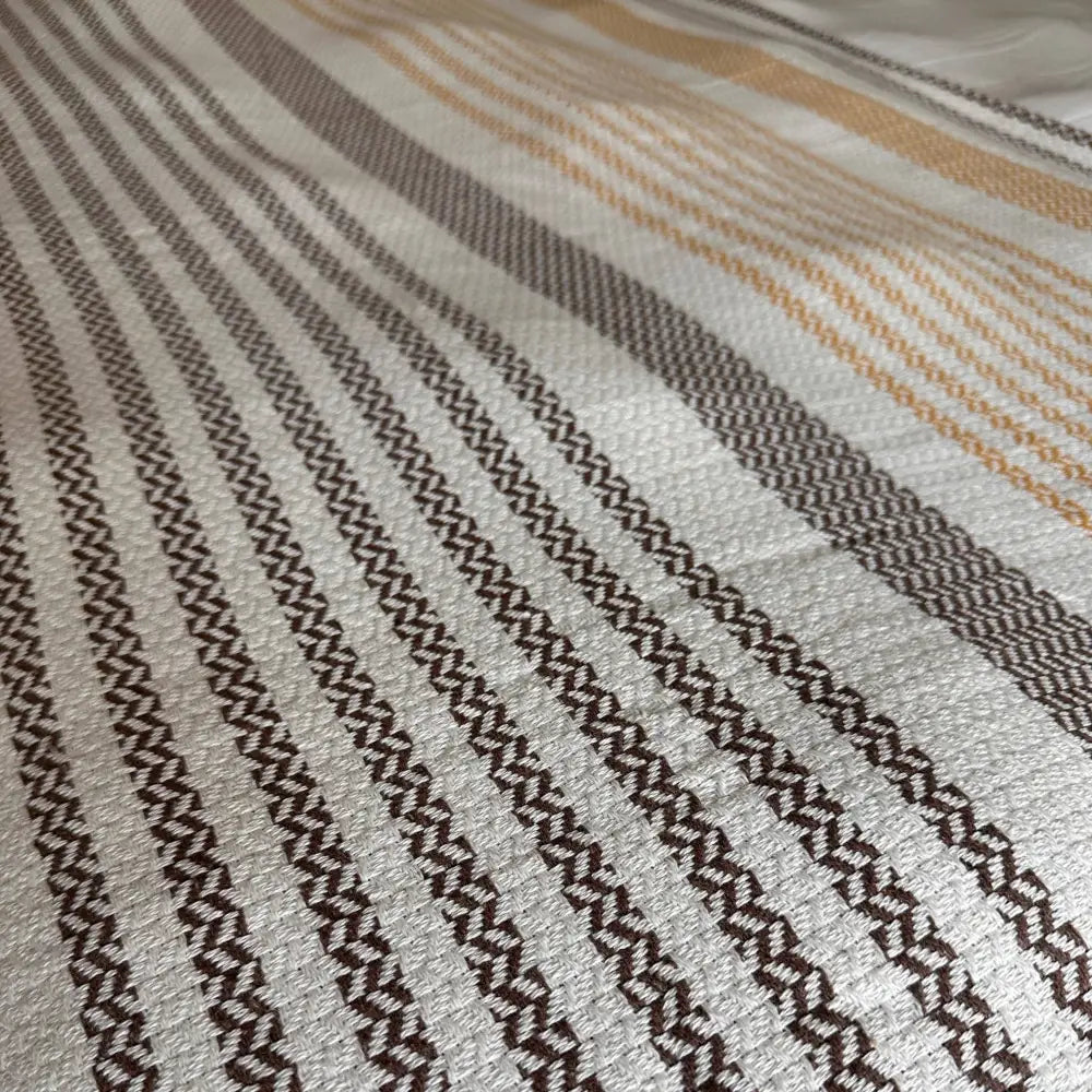 Close-up of striped Turkish cotton bed blanket with pom pom tassels in brown and orange