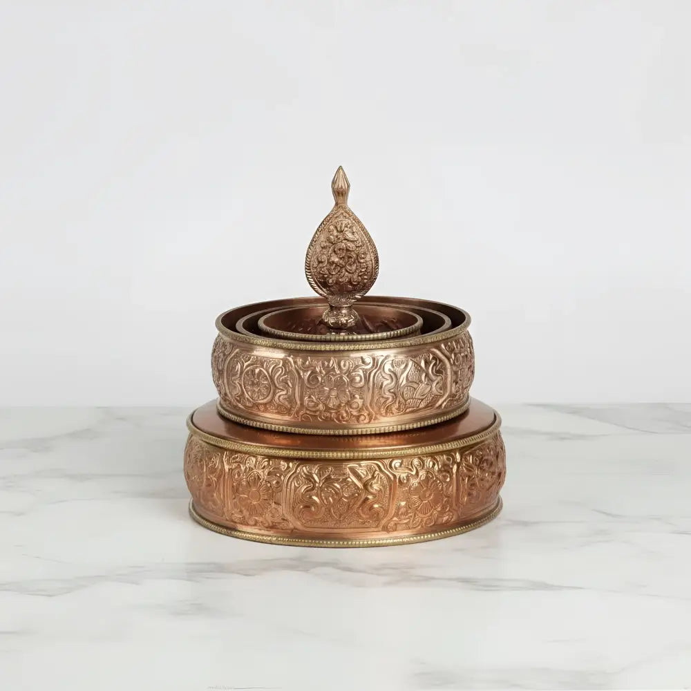 A copper-colored traditional tibetan buddhist offering mandala set featuring an intricately engraved prayer wheel with finial
