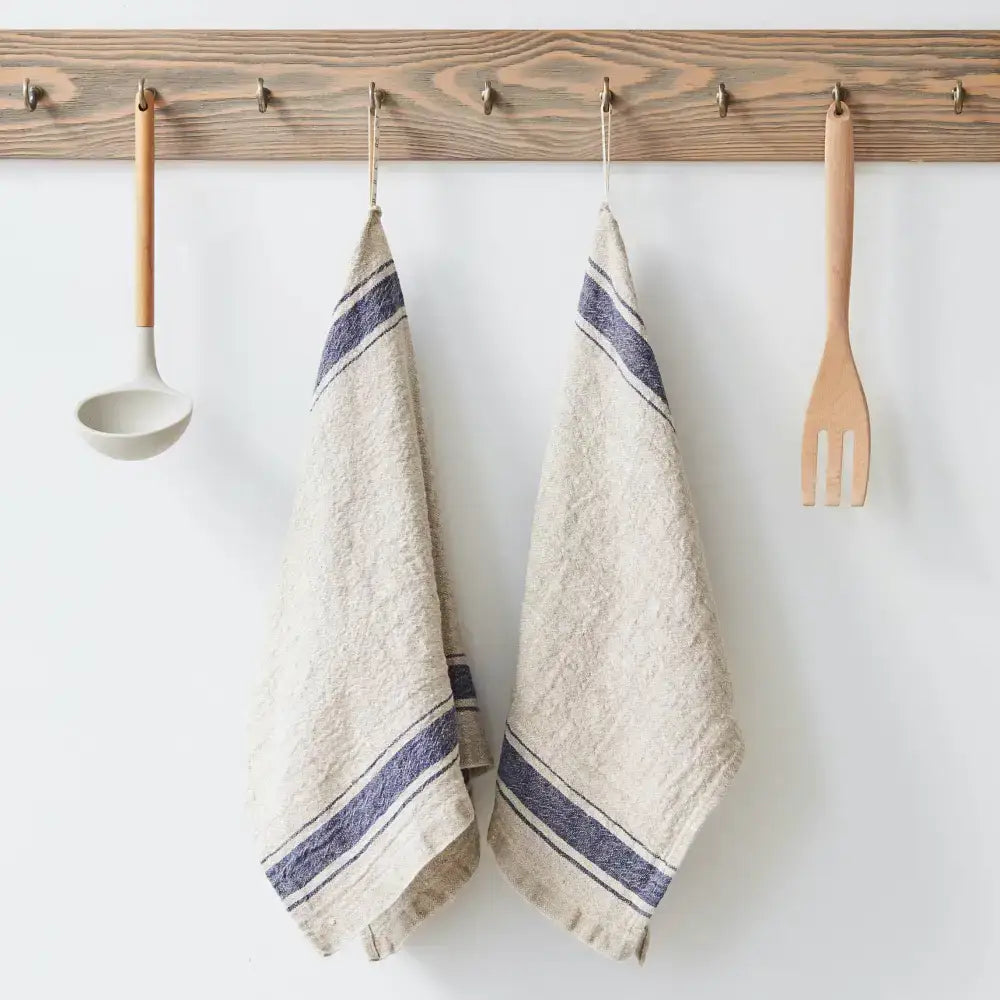 A natural color kitchen towel with blue stripes hanging on a hook next to kitchen utensils.