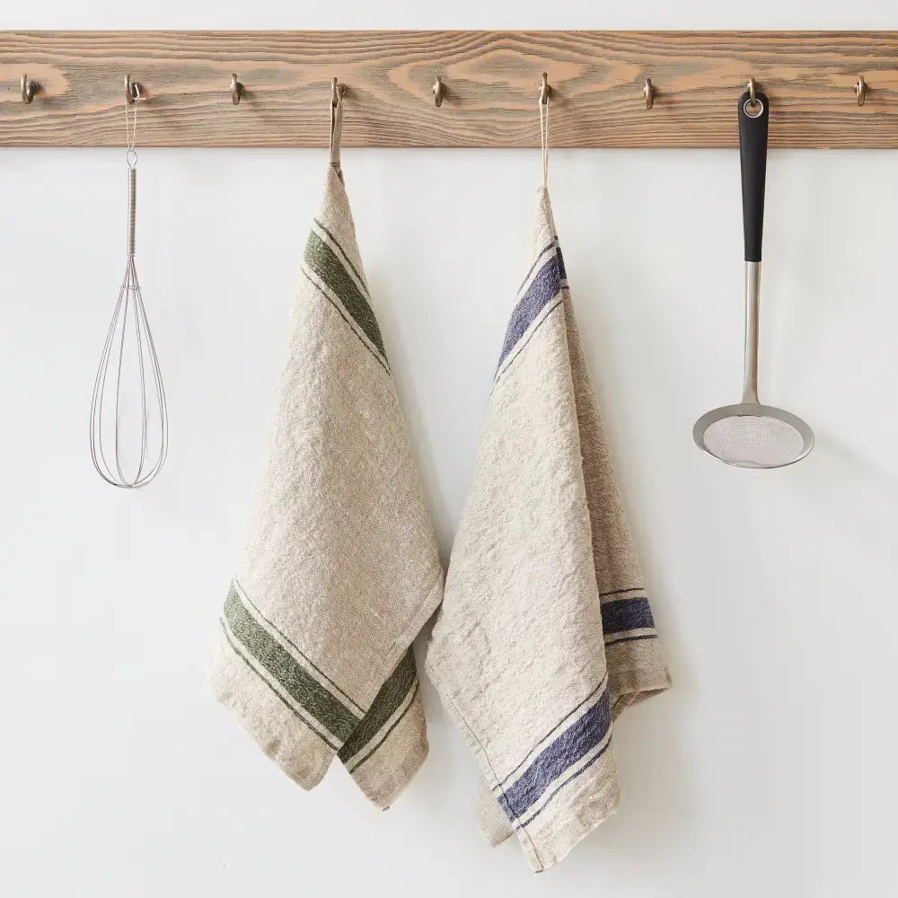 A natural color kitchen towel with green and blue stripes hanging on a hook next to kitchen utensils.