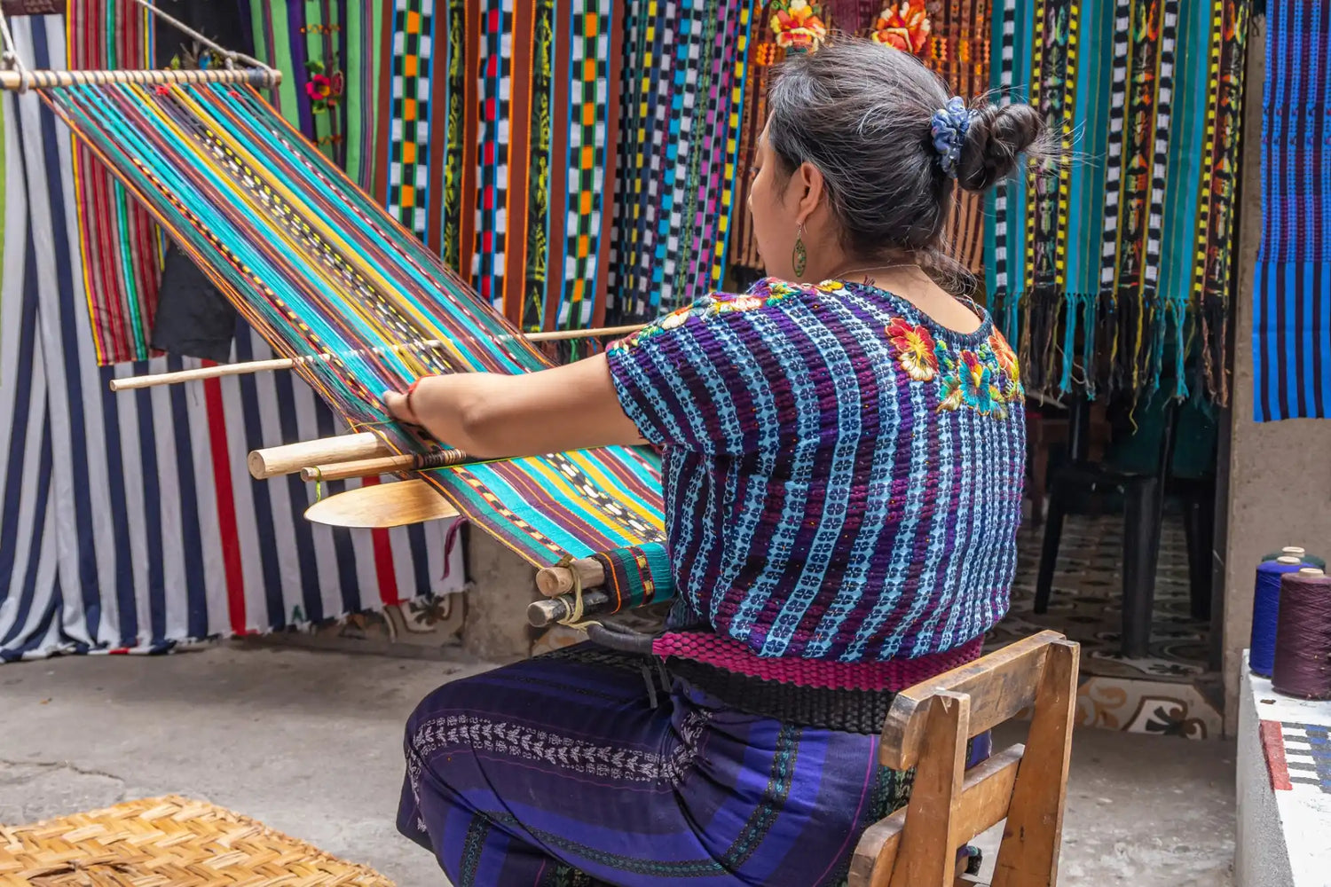 Woman weaving a colorful textile on a backstrap loom.