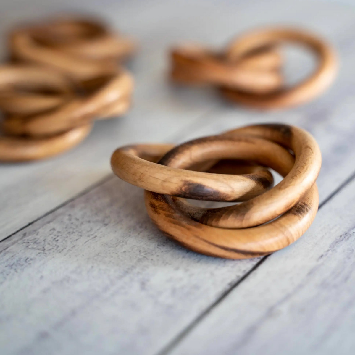 A close up of an interlocking wooden napkin ring with three others in a blurred background.