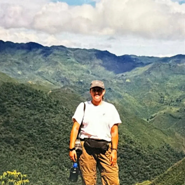 A person wearing a handmade white t-shirt and khaki pants stands amid green mountains exploring eco-friendly woven textiles