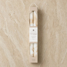 A set of 12 off-white decorative taper candles with gold metallic swirls in a minimalist beige cardboard sleeve