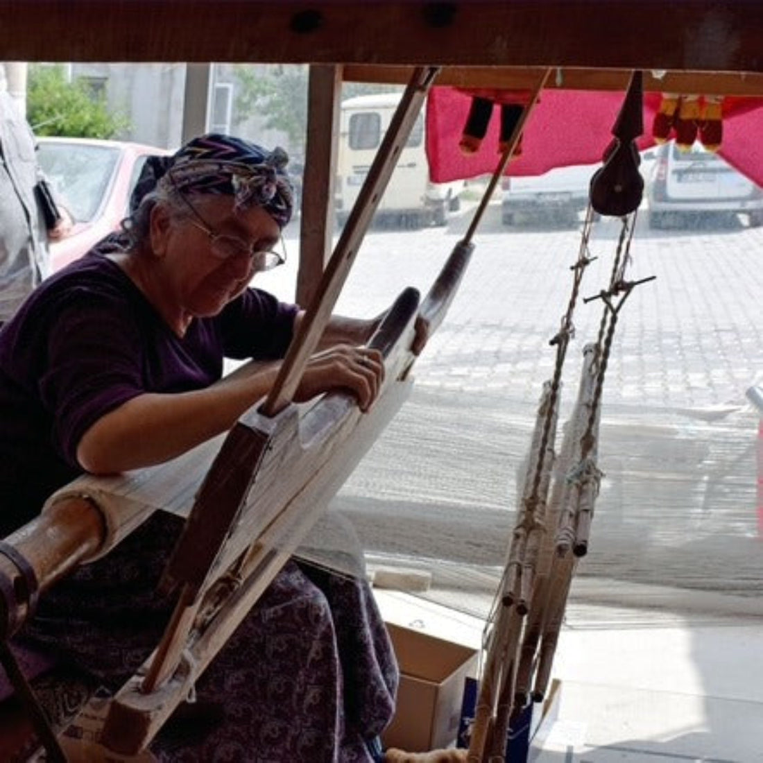 Person weaving on a loom with a view of a street outside