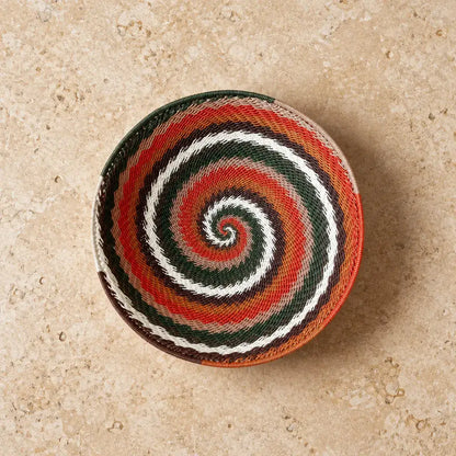 A handwoven african zulu wire bowl with a vibrant red white green and orange spiral made from recycled telephone wire