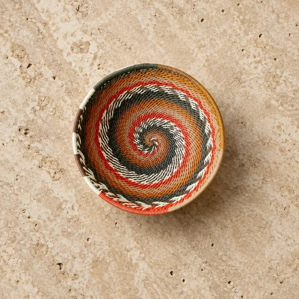 A colorful african zulu wire bowl handwoven from recycled telephone wire with vibrant orange red black white and brown spiral strands