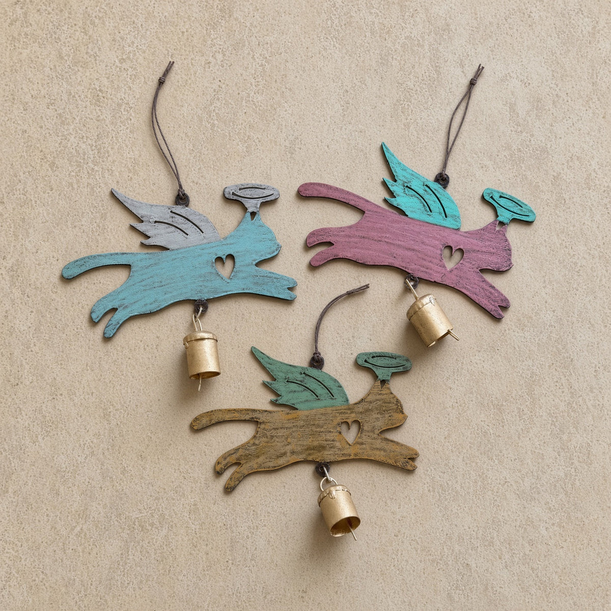 Three hand-painted wooden angel cat bell ornaments with rust patina, wings, heart cutouts, and small brass bells