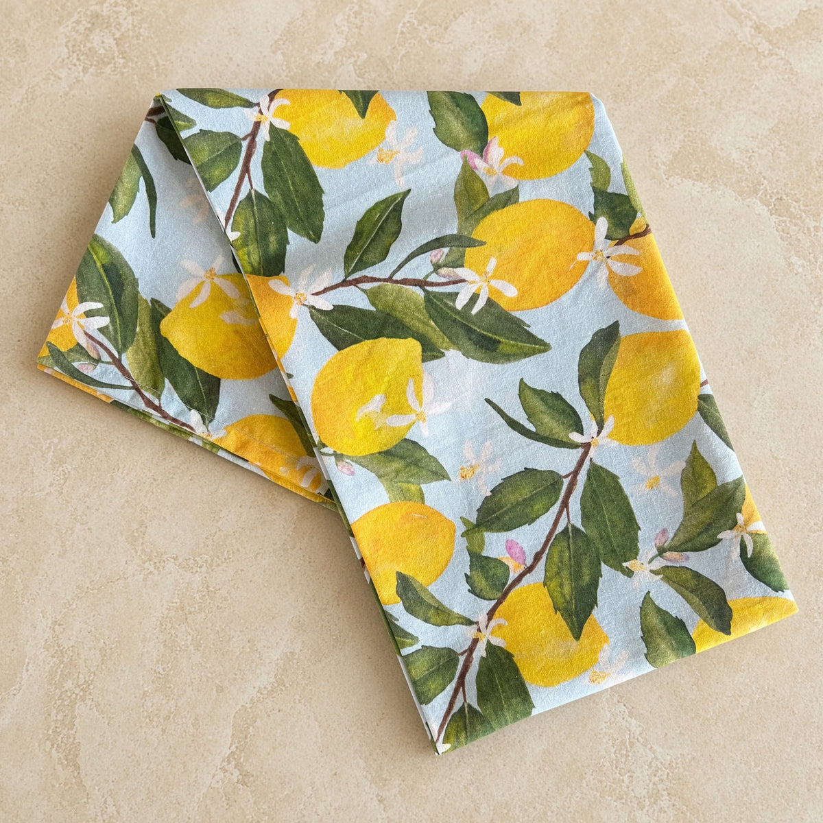 Folded artisan tea towel with pre-washed flour sack fabric featuring watercolor lemons and delicate blossoms on blue background