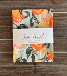 Folded pure cotton handmade tea towel with vibrant orange watercolor print and green leaves on light gray background