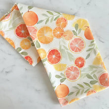 Folded artisan tea towel with watercolor print of orange grapefruit and lemon on off white flour sack fabric