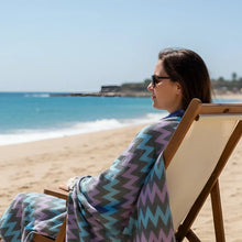A woman wrapped in an authentic turkish organic cotton beach towel with blue fuchsia and gray zigzag pattern