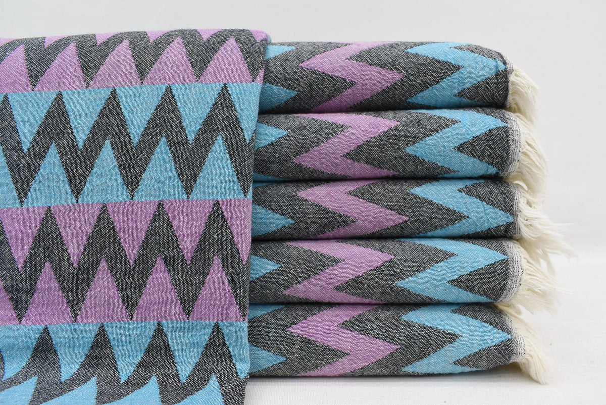 Stack of folded organic bath towels with bold purple teal and black zigzag pattern perfect for beach use