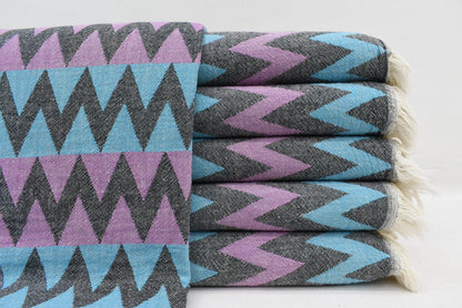 Stack of folded organic bath towels with bold purple teal and black zigzag pattern perfect for beach use