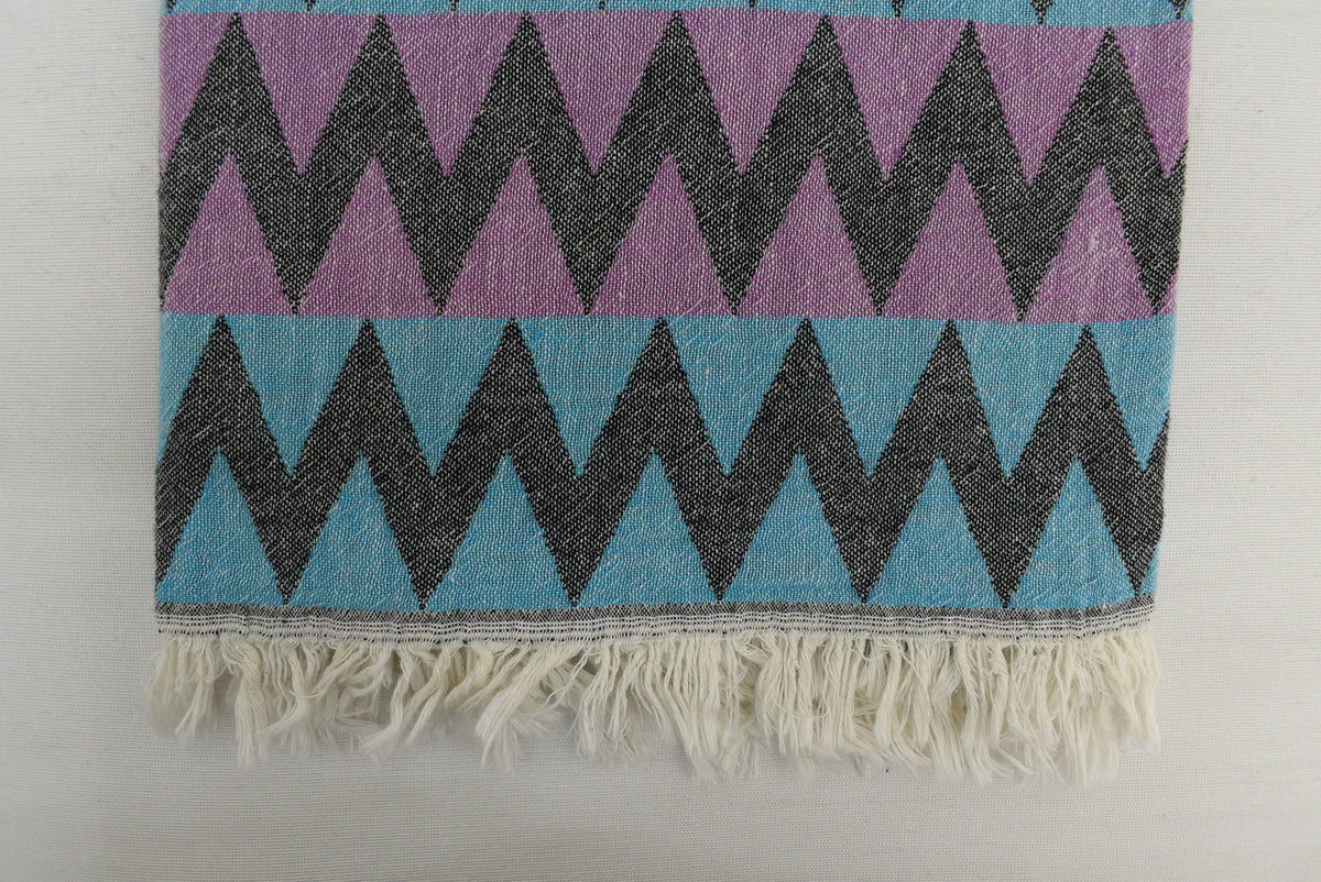 A vibrant purple and teal organic bath towel with zigzag pattern and fringed edge perfect for beach use