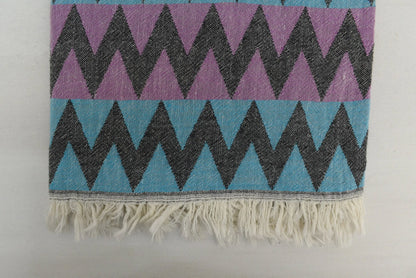 A vibrant purple and teal organic bath towel with zigzag pattern and fringed edge perfect for beach use