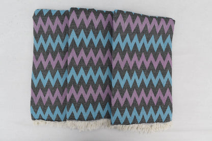 Folded organic bath towel with bold purple and light blue zigzag pattern and white fringed edges for beach use