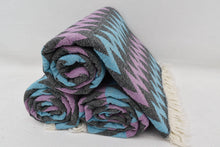 A rolled organic bath towel with a bold purple blue gray zigzag pattern and white fringe perfect for beach use