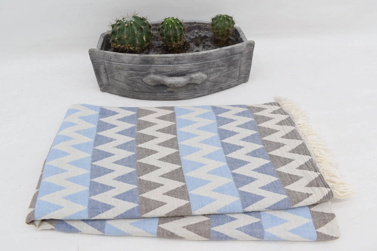A folded organic turkish towel beach towel in light blue gray and white zigzag pattern with fringed edges 36x78