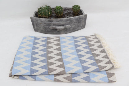 A folded organic turkish towel beach towel in light blue gray and white zigzag pattern with fringed edges 36x78
