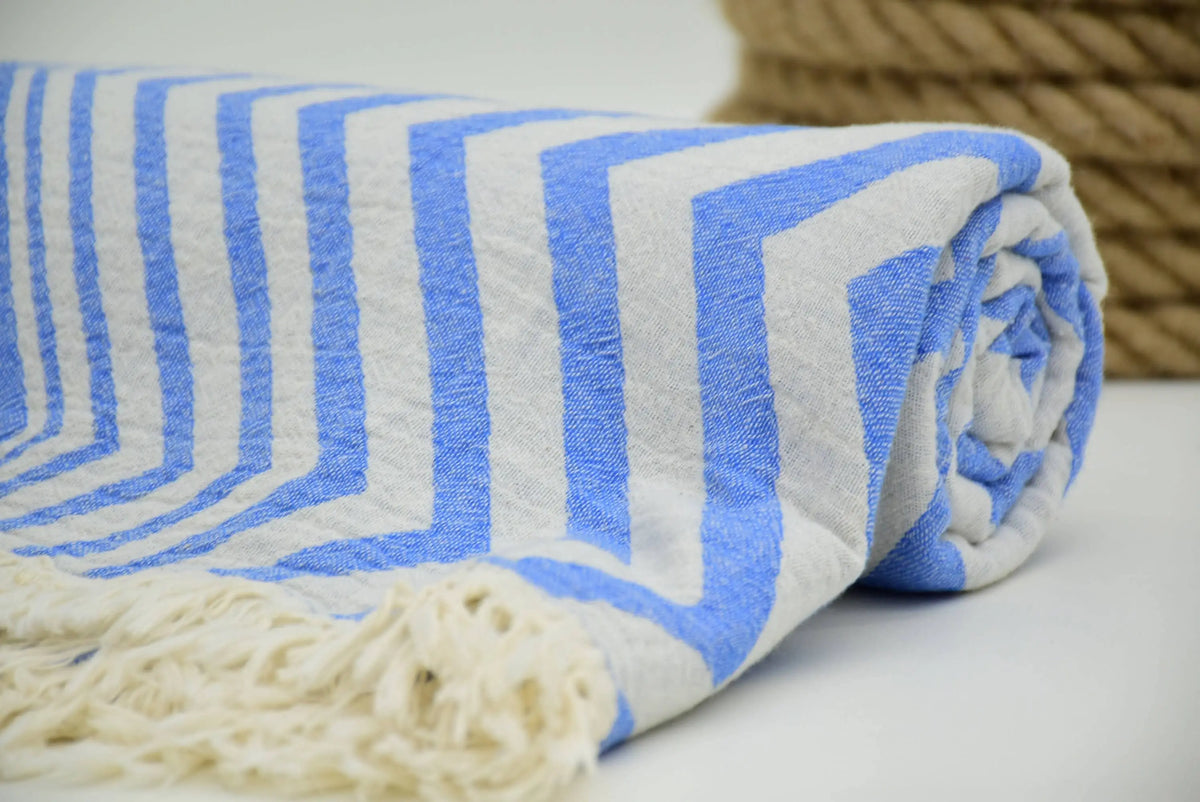 A rolled turkish towel with zigzag design pale sax blue stripes and cream-colored fringe in soft cotton material