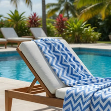 Blue and white chevron patterned authentic turkish organic cotton beach towel draped over wooden lounge chair by pool