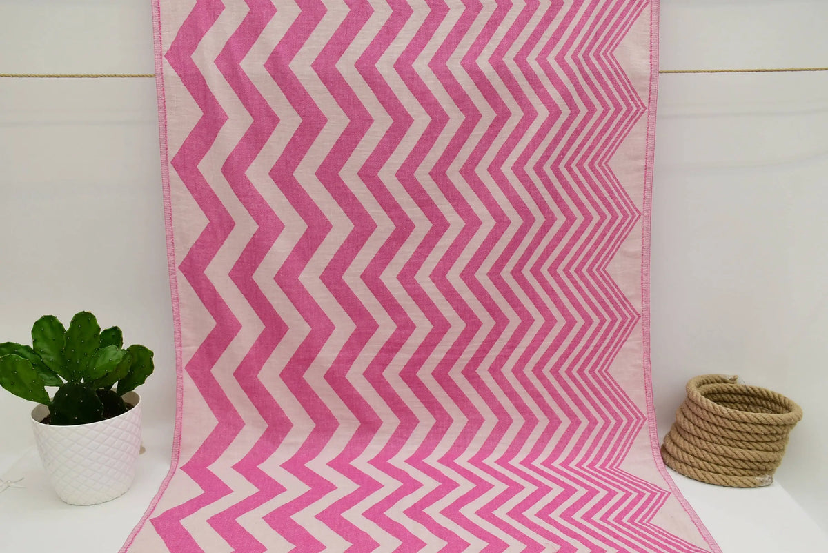 A vibrant pink and white zigzag pattern peshtemal towel with a soft textured weave perfect for beach or bath use