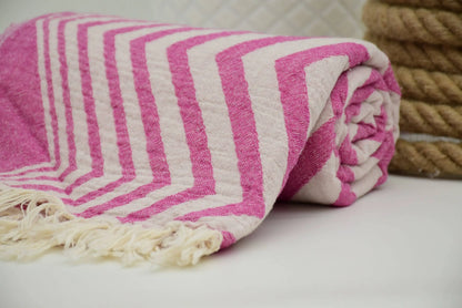 A rolled pink and white striped zigzag pattern peshtemal towel with textured weave and fringed edges