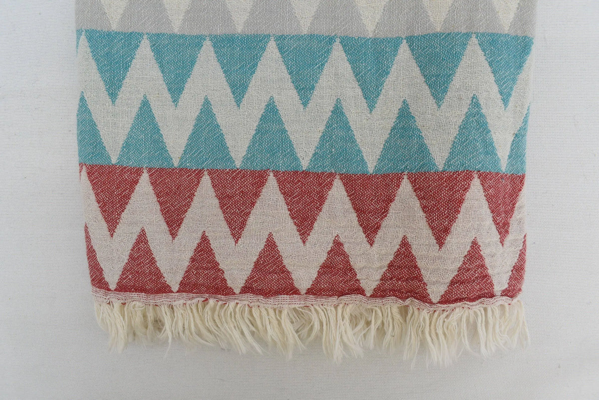 A woven organic turkish towel beach towel with teal coral cream zigzag pattern and soft fringed edges