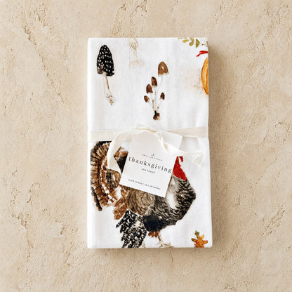 White thanksgiving tea towel with detailed turkey mushrooms autumn leaves paired with african zulu trivet nest