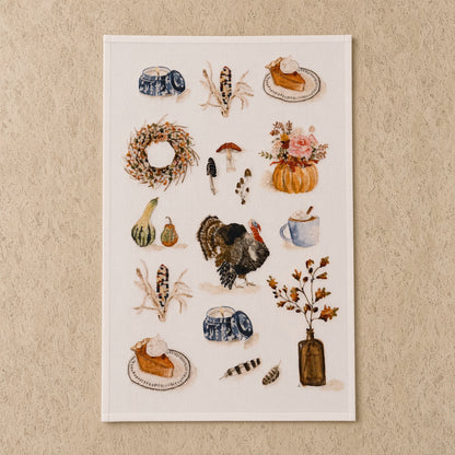 A rectangular autumn tea towel with watercolor turkey pumpkins and pie paired with an african zulu trivet nest