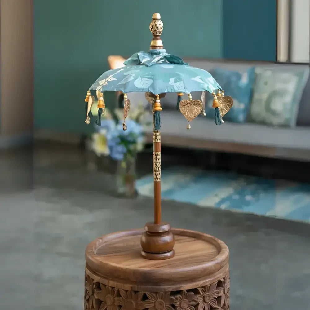 Delicate turquoise balinese tabletop umbrella with gold heart tassels and wooden handle on carved stand for grace temple ceremonies ornamental parasols