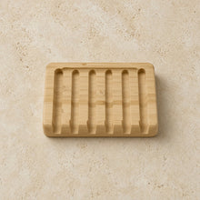 Light-colored bamboo soap lift with six vertical slots and lattice design allows quick drainage and drying