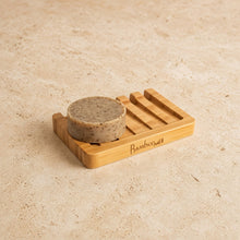 A light brown bamboo soap lift with lattice design allows drainage holding a round speckled beige soap bar from bamboosweet